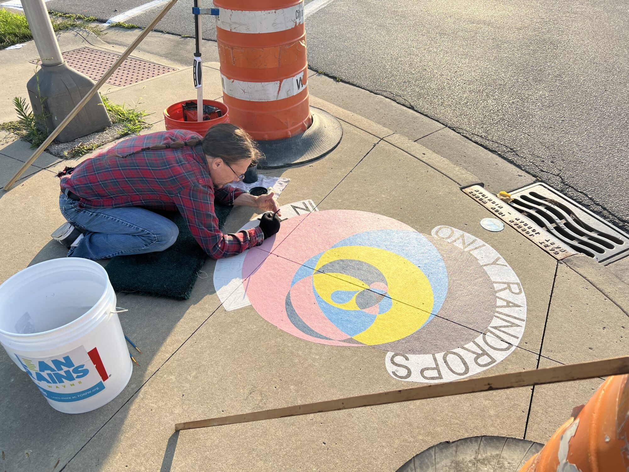 Picture of artist painting a Clean Drains mural that says "Only Raindrops in the Drain".