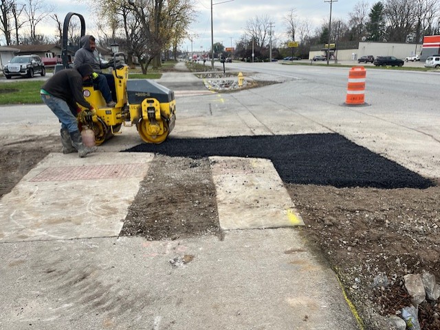 Photo of a crew rolling new asphalt to patch a hole.