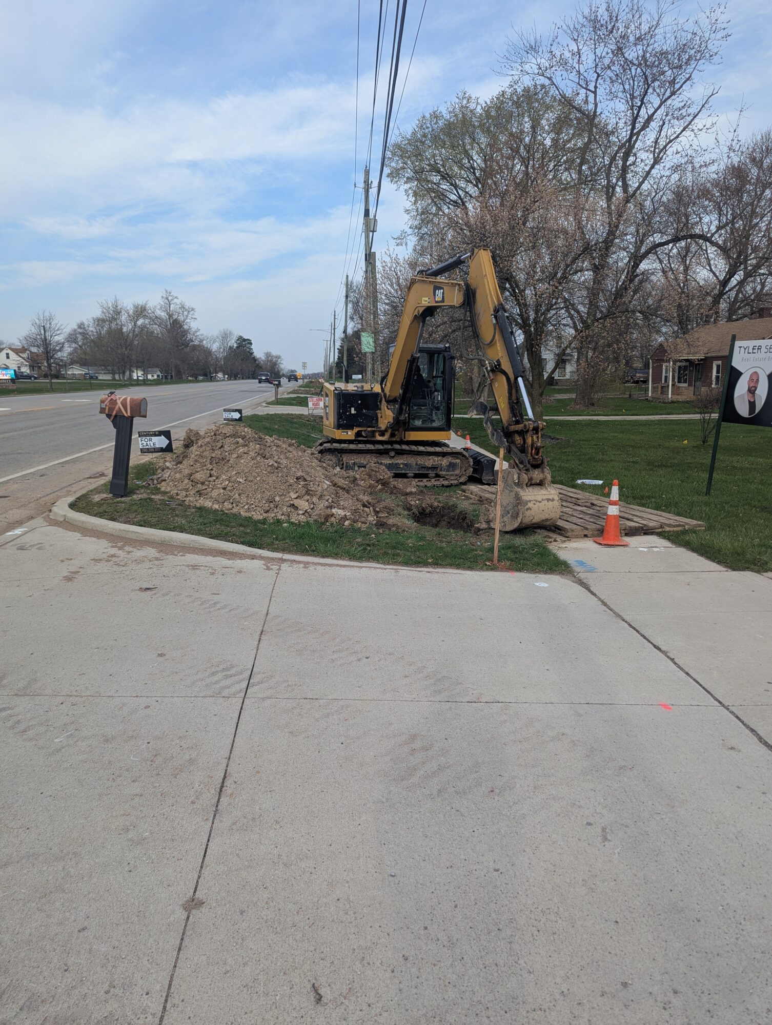 A bulldozer digging up grass to begin working on utility work at the corner of a sidewalk in a neighborhood.