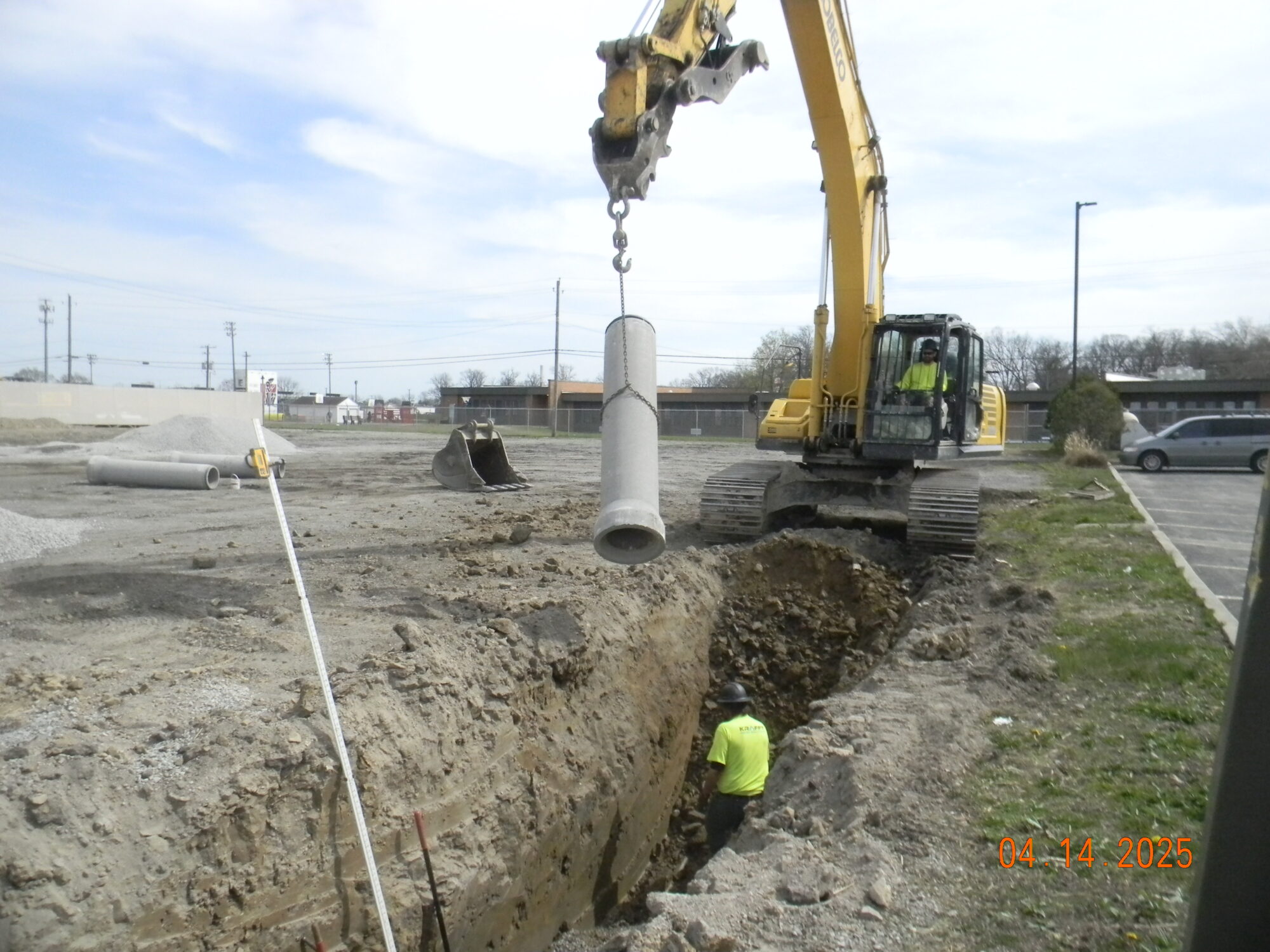 Bulldozer holding a pipe that is being placed into dug up ground.