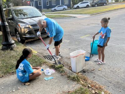 IMG_6392 A family, one man and two kids, picking up trash around a drain in a neighborhood.