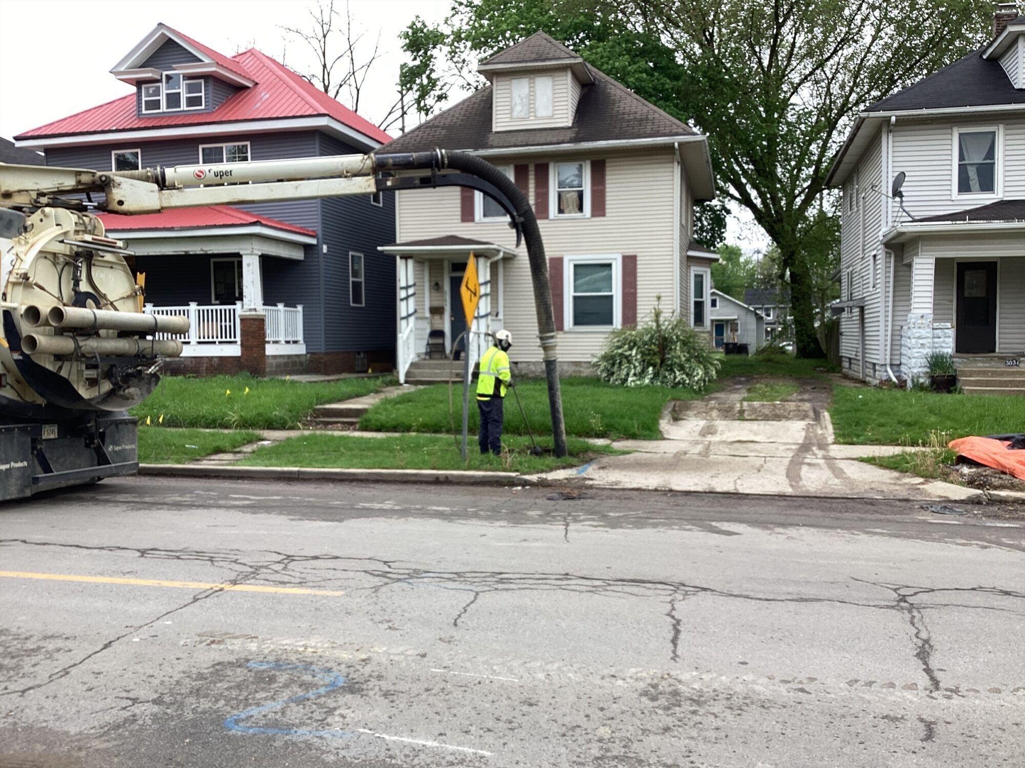 The picture shows three houses and a utility truck performing a lead line replacement while a construction member observes.