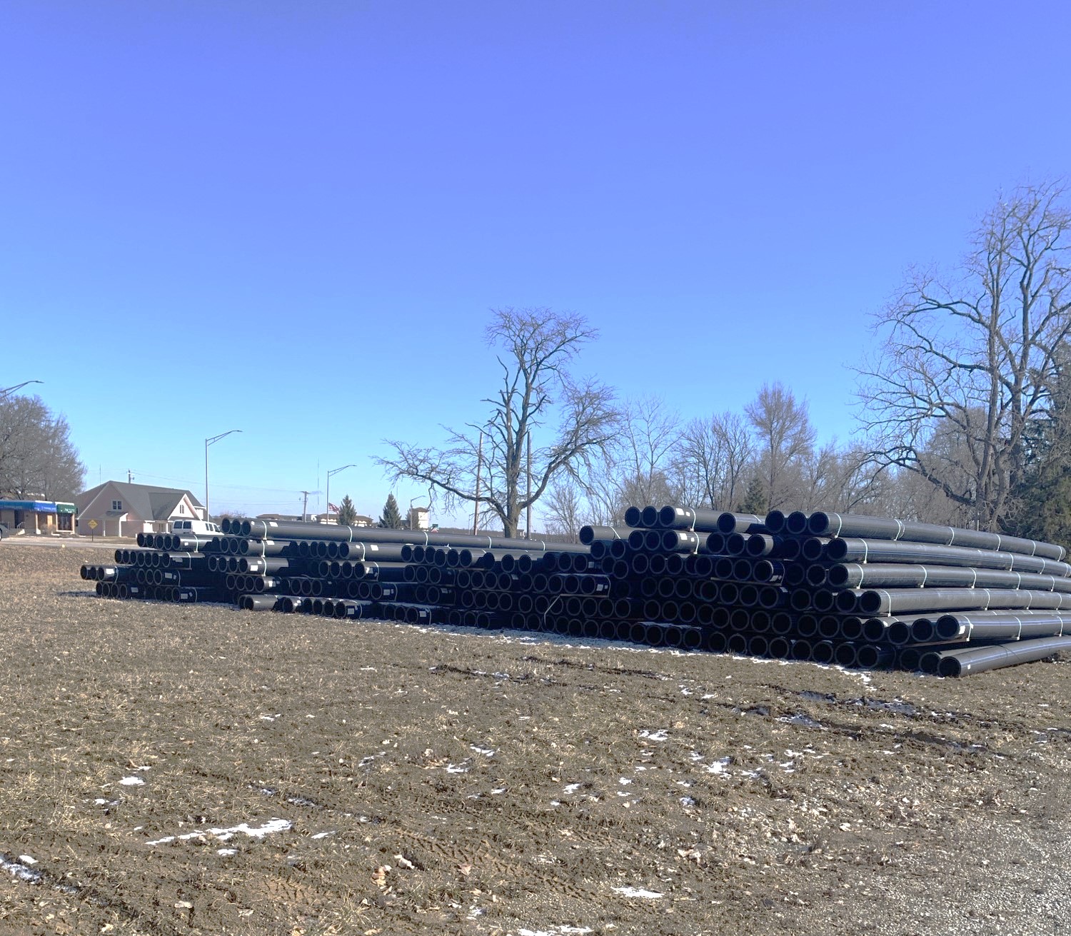 A stack of polyethelene water main pipe in a field of grass.