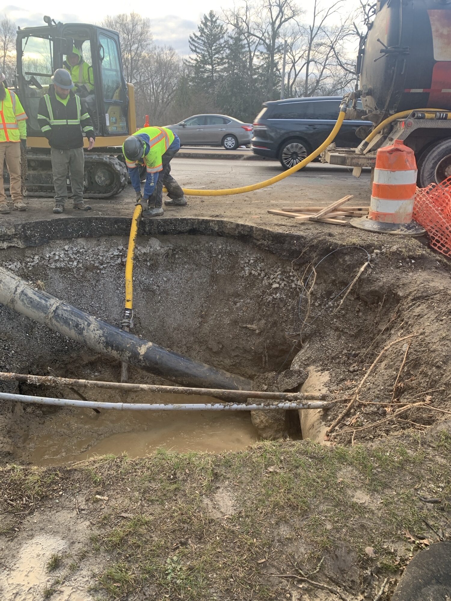 Workers working with vacuum on a busy street, draining out stillwater in construction hole.