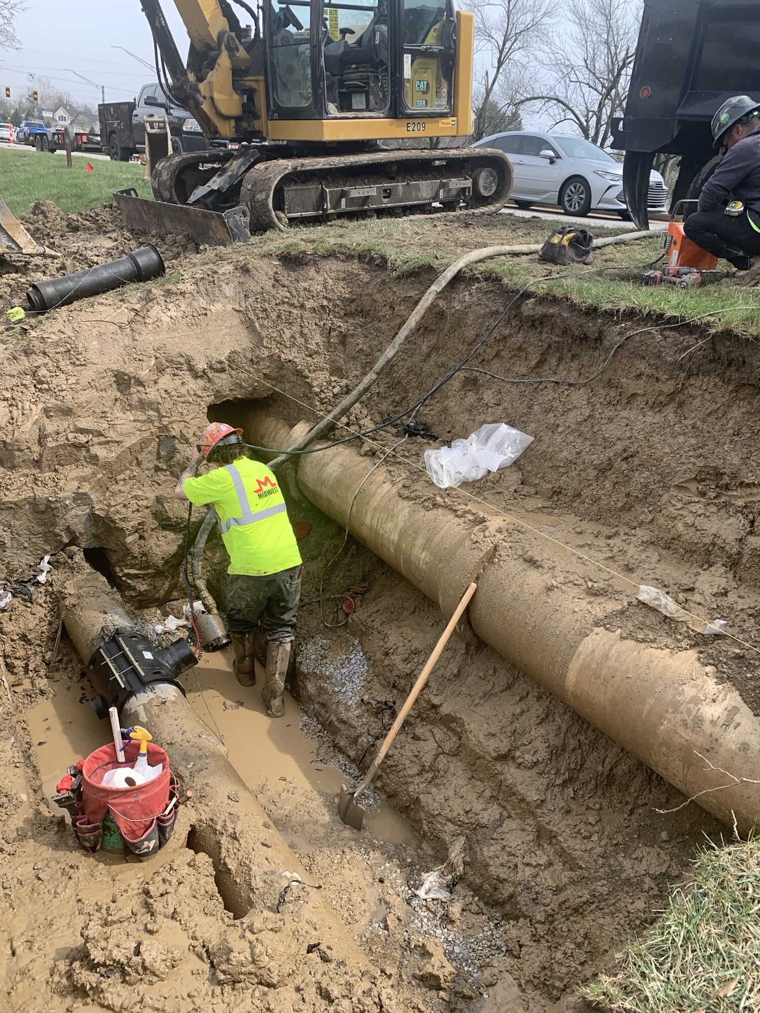Crew worker in dug out pit along construction site, surrounding by construction equipment and water pipe.