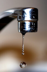 Close-up of a metal faucet with a single drop of water hanging from the spout, suggesting a dripping tap.